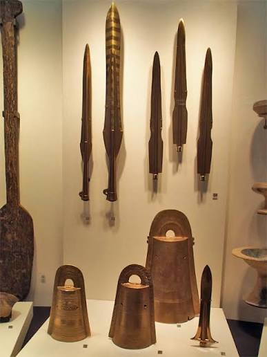 Actual excavated bronze swords and bronze bells on display, with many swords lined along a wall