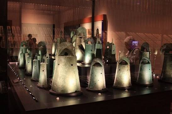 Numerous actual bronze bells arranged neatly inside a glass display case
