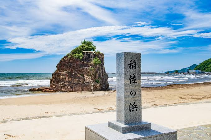 A stone marker inscribed 'Inasa Beach,' with Bentenjima visible beyond it